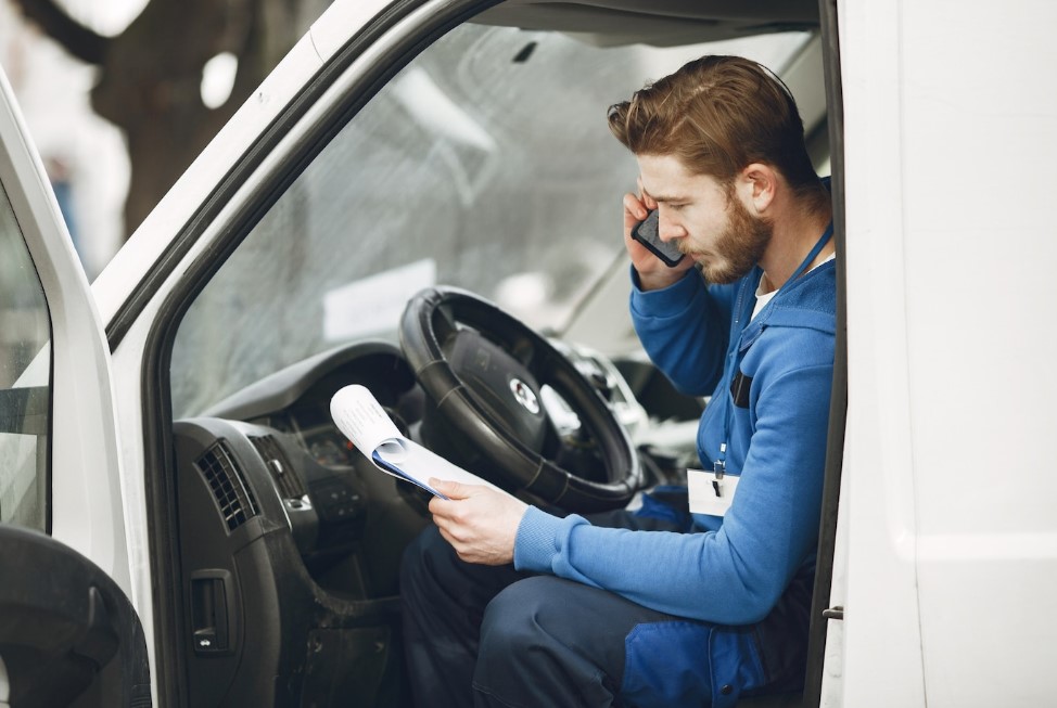 мужчина в салоне грузового автомобиля разговаривает по телефону и смотрит на документы